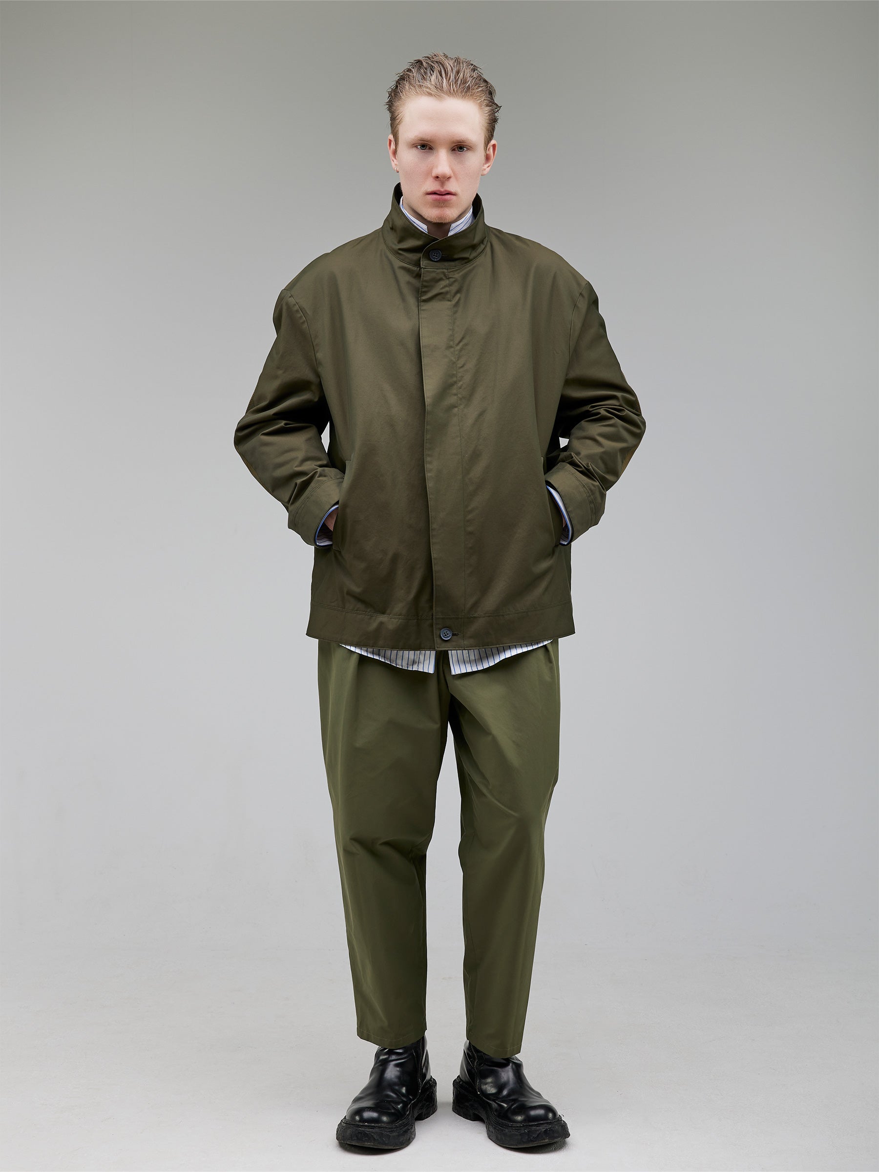 A lightweight technical jacket with dropped shoulders and mesh elbow accents.
Outer: 58% Cotton, 38% Polyamide Gabardine with a light PU finish in army green
Closure: 8mm gunmetal zipper
Styled with an oversized striped mandarin-collar shirt and tapered trousers.