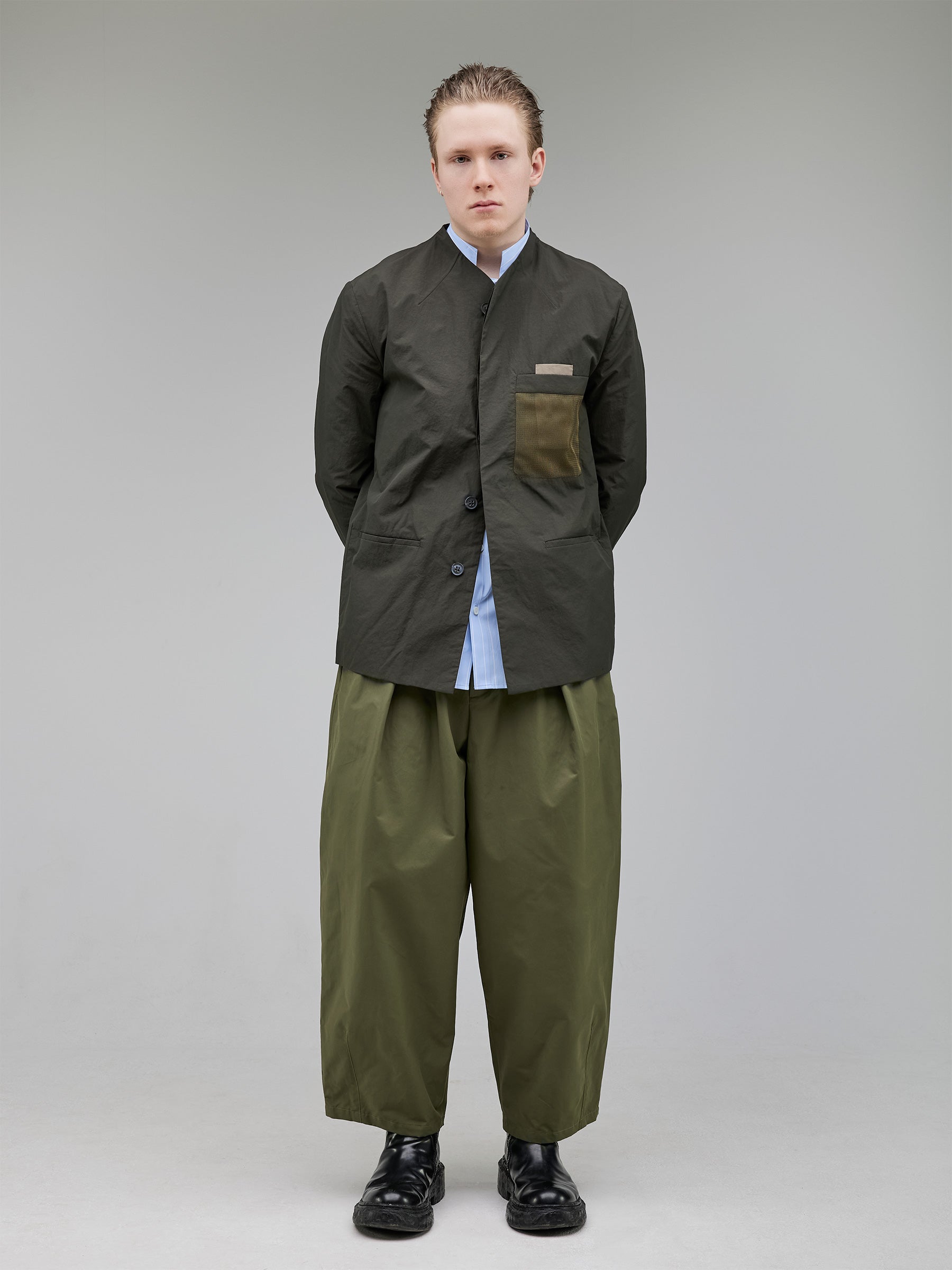 A tailored, collarless blazer with concealed closures and structured contrast chest pockets, balancing minimalism and technical precision.
Shirt: Baby blue striped mandarin-collar shirt, regular fit.
Bottom: Wide-leg pleated trousers with darted shaping for movement.