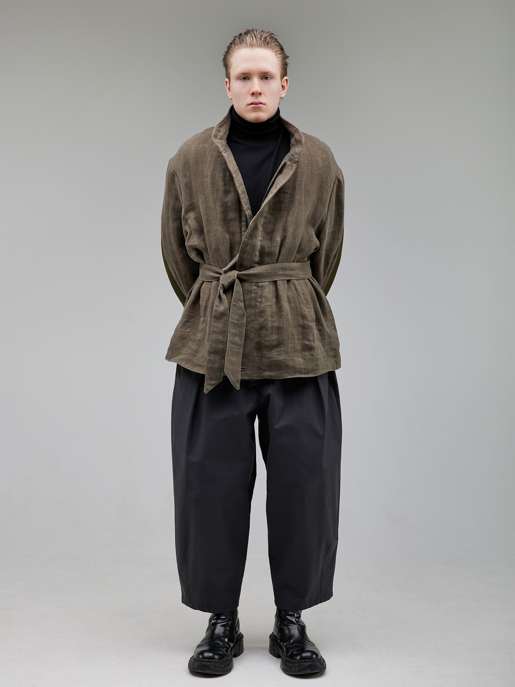 A belted oiled linen jacket with a collarless construction and sleeve tab details. Water-resistant for function and longevity.
Lining: 100% Recycled Polyester (GRS-certified)
Paired with wide-leg pleated trousers for a relaxed yet structured look.