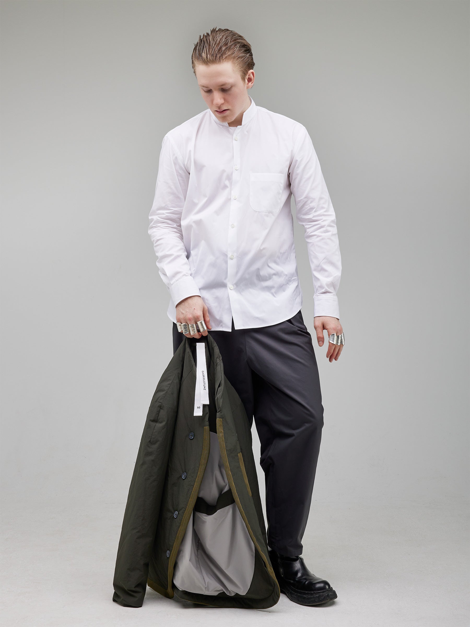 Oversized white mandarin-collar shirt with rounded trousers, complemented by a technical puffer with mesh details and darted shaping, carried by hand for an adaptable styling approach.