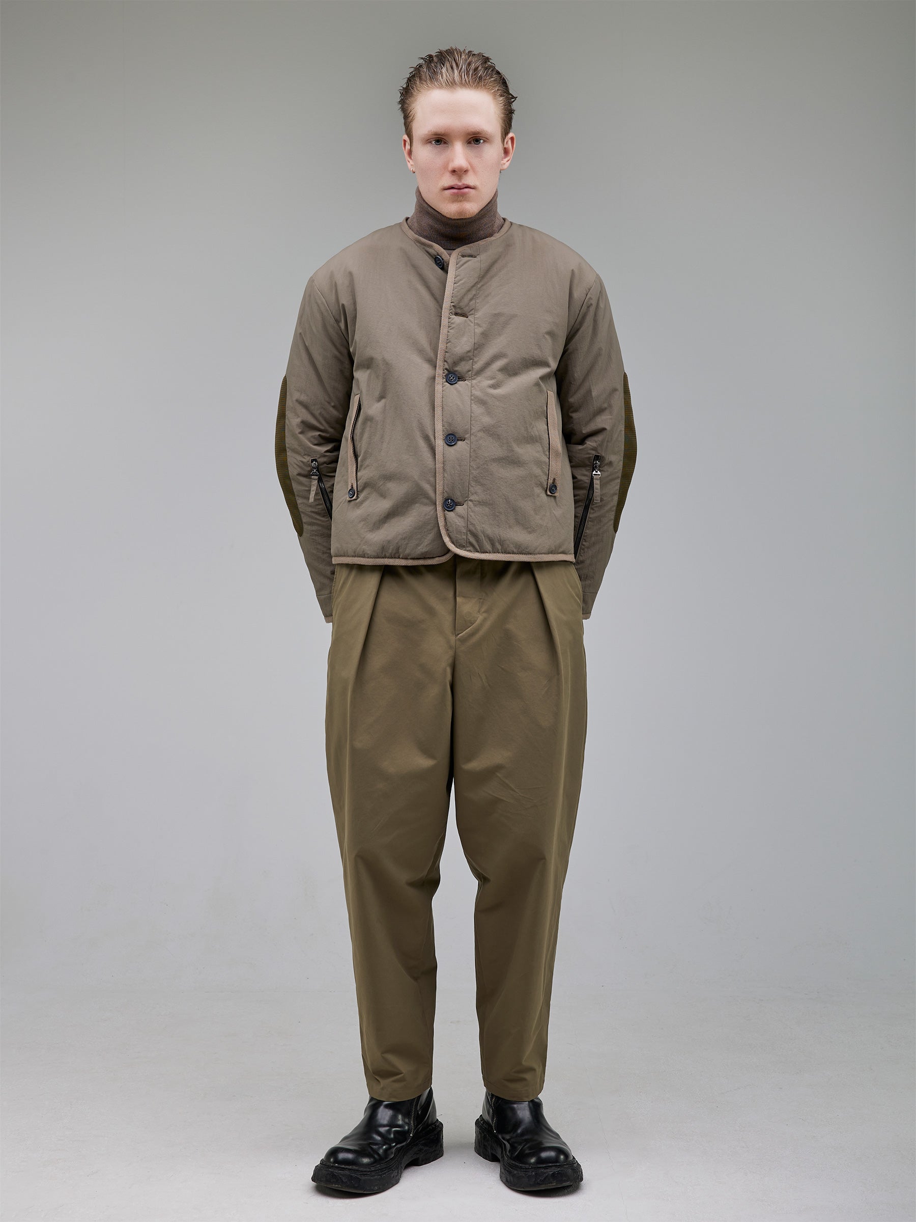 Lightweight insulated liner with a down-like feel, enhanced with mesh elbow details and contrast tape accents. Functional elements include vintage horn button closure and dual zippered lower-arm pockets.
Outer: 100% Recycled Polyamide
Lining: 100% Recycled Polyester (GRS-certified)
Fill: 60% Recycled PET, 40% Polyamide – sustainable down alternative
Details: 100% Recycled Cotton tape trim
Bottom: Tapered trousers with a rounded leg, featuring front pleats and a tailored waistband with button closure.