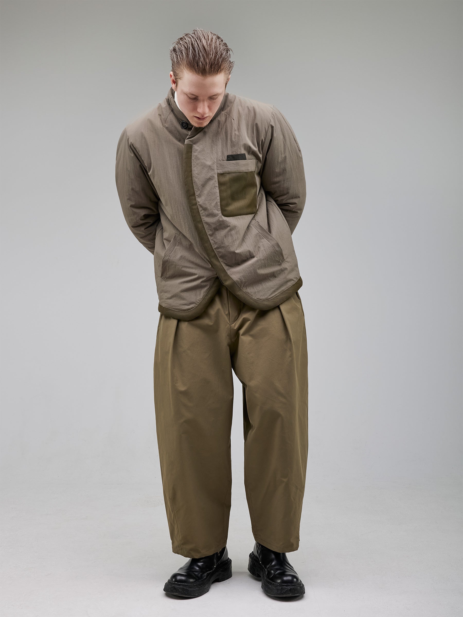 A collarless puffer jacket with structured darting for a precise fit. Mesh details on the pocket and hem add a contemporary edge, while hidden closures and contrast chest pockets enhance its minimalist aesthetic.
Outer: 100% Recycled Polyamide
Lining: 100% Recycled Polyester (GRS-certified)
Fill: 60% Recycled PET, 40% Polyamide – high-performance insulation
Details: 100% Recycled Cotton tape accents
Bottom: Wide-leg pleated trousers with a tailored waistband and sculpted hem darts.
Fabric: 64% Cotton,