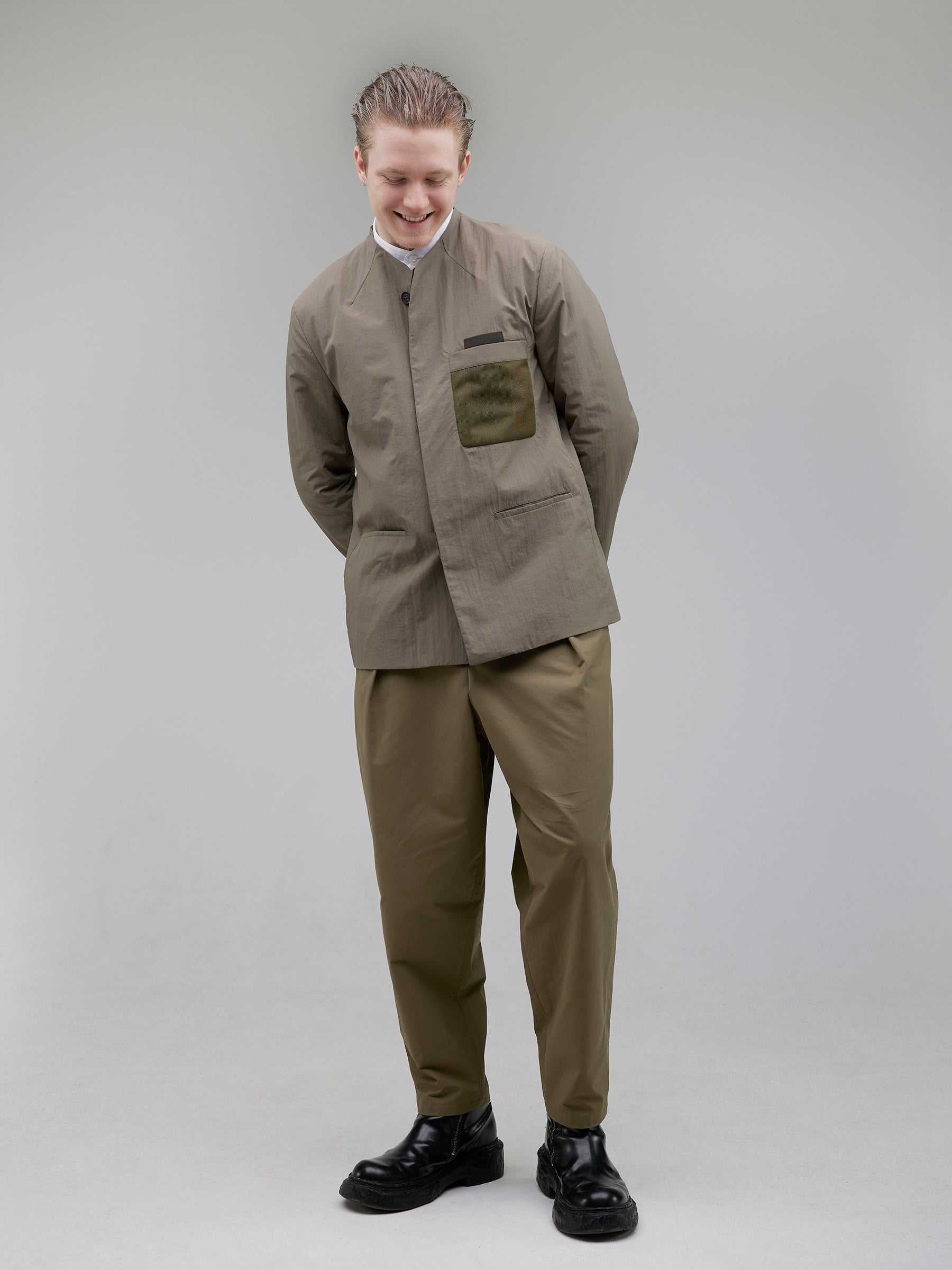 A tailored technical blazer with mesh detailing on the chest pocket, hidden welt closures, and contrast pocket accents. The collarless silhouette is shaped with structured darting for a precise, contemporary fit.
Outer: 100% Recycled Polyamide
Lining: 100% Recycled Polyester (GRS-certified)
Closure: Vintage-finish horn buttons
Shirt: White mandarin-collar shirt with a sharp, tailored fit.
Fabric: 100% Cotton
Buttons: White Trocas Mother of Pearl
Bottom: Rounded trousers with a tailored waistband and