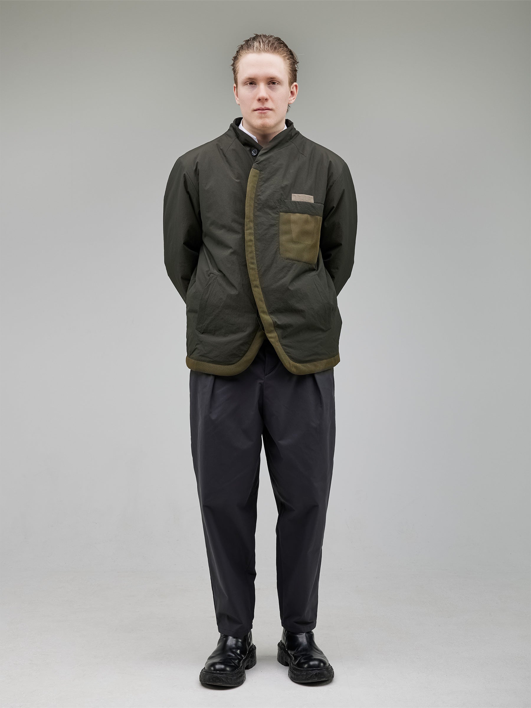 A collarless puffer jacket with structured darting for a precise fit. Mesh details on the pocket and hem add a contemporary edge, while hidden closures and contrast chest pockets enhance its minimalist aesthetic.
Outer: 100% Recycled Polyamide
Lining: 100% Recycled Polyester (GRS-certified)
Fill: 60% Recycled PET, 40% Polyamide – high-performance insulation
Details: 100% Recycled Cotton tape accents
Bottom: Wide-leg pleated trousers with a tailored waistband and sculpted hem darts.
Fabric: 64% Cotton,