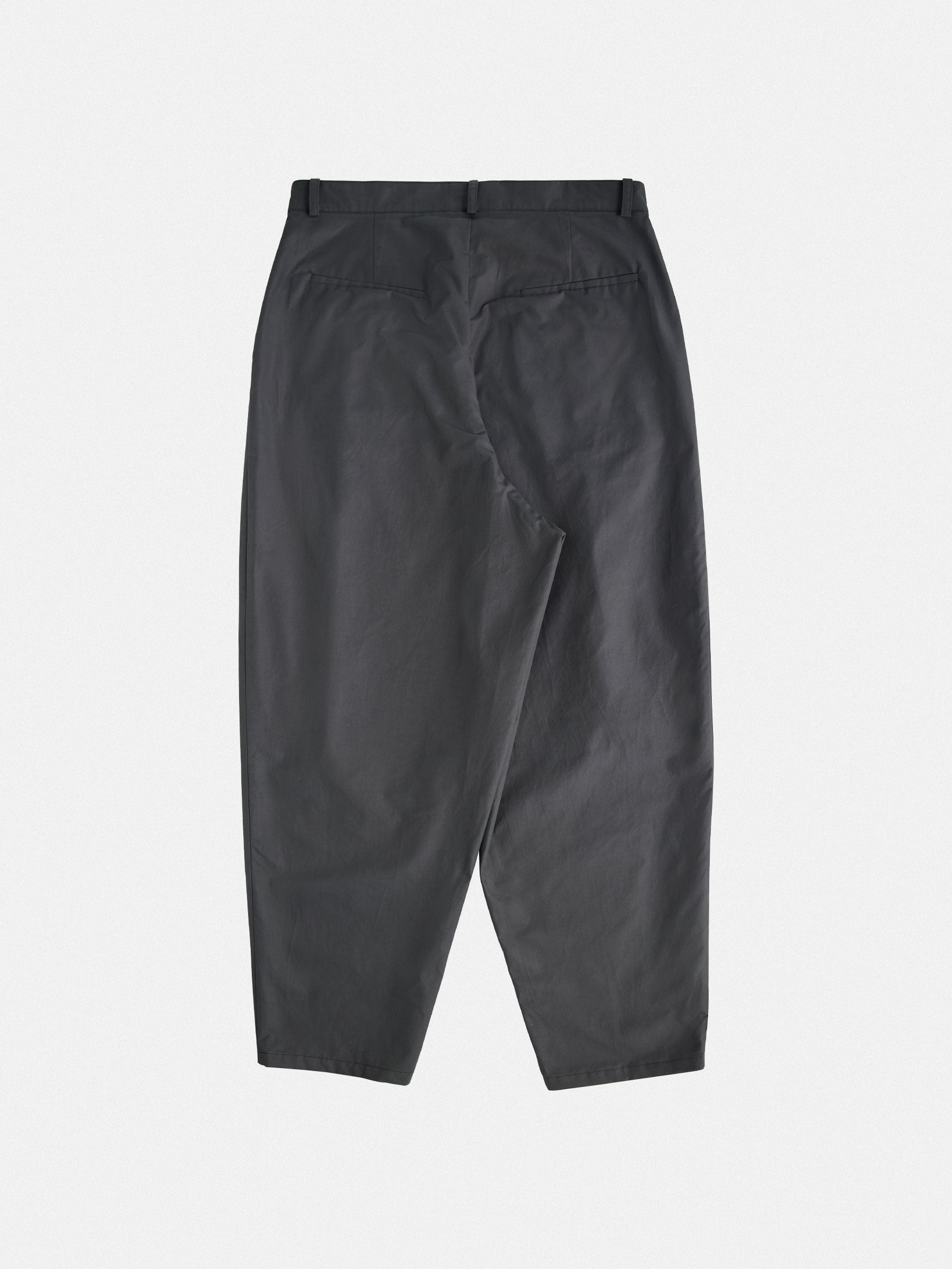 Tapered trousers with a rounded leg, featuring front pleats and a tailored waistband with button closure.