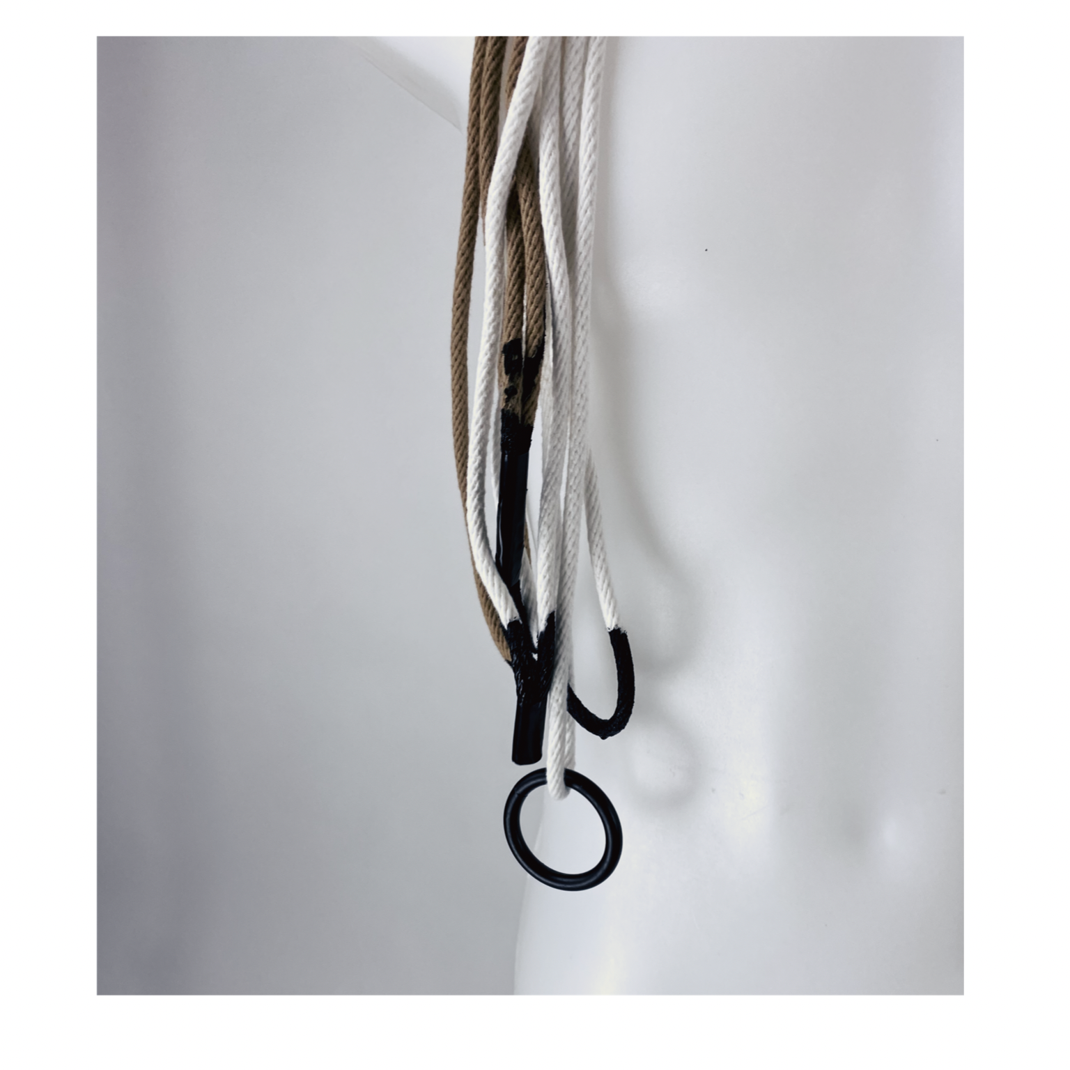 Close-up of white and beige ropes intertwined and hanging from a black hook against a plain white background.