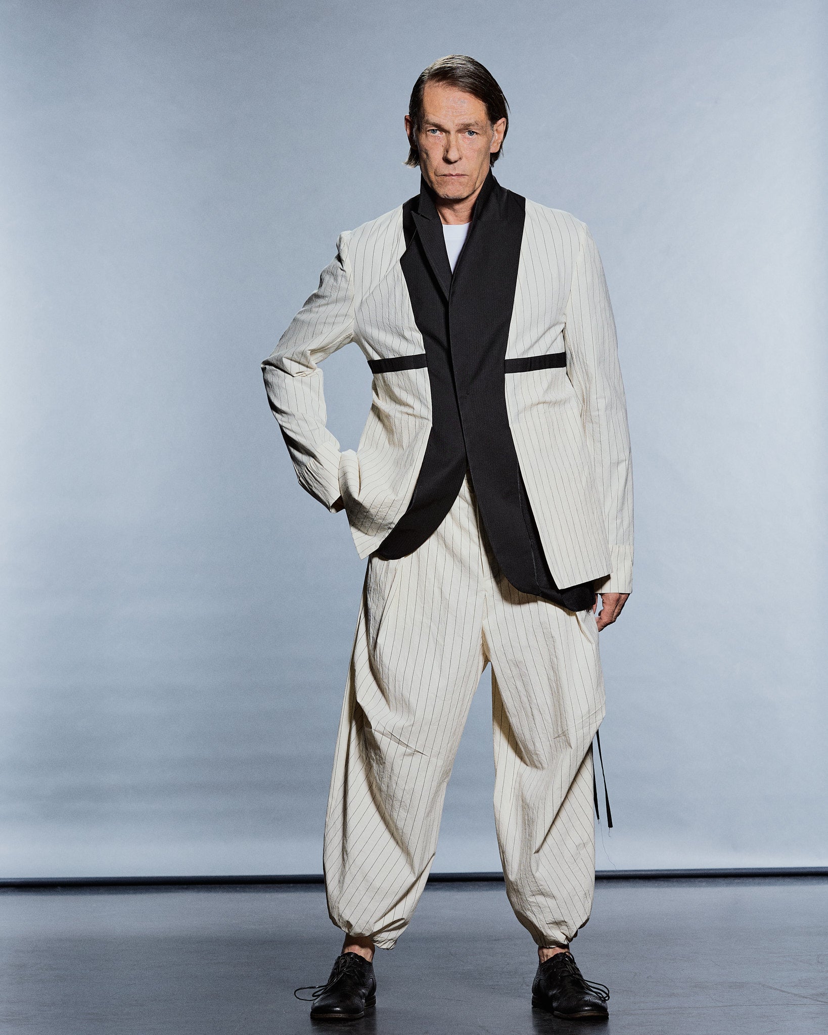 Full-length cream pinstripe jacket with contrasting black shawl panel and tapered cuffed trousers — GABRIELSTUNZ APLOMB SS27.