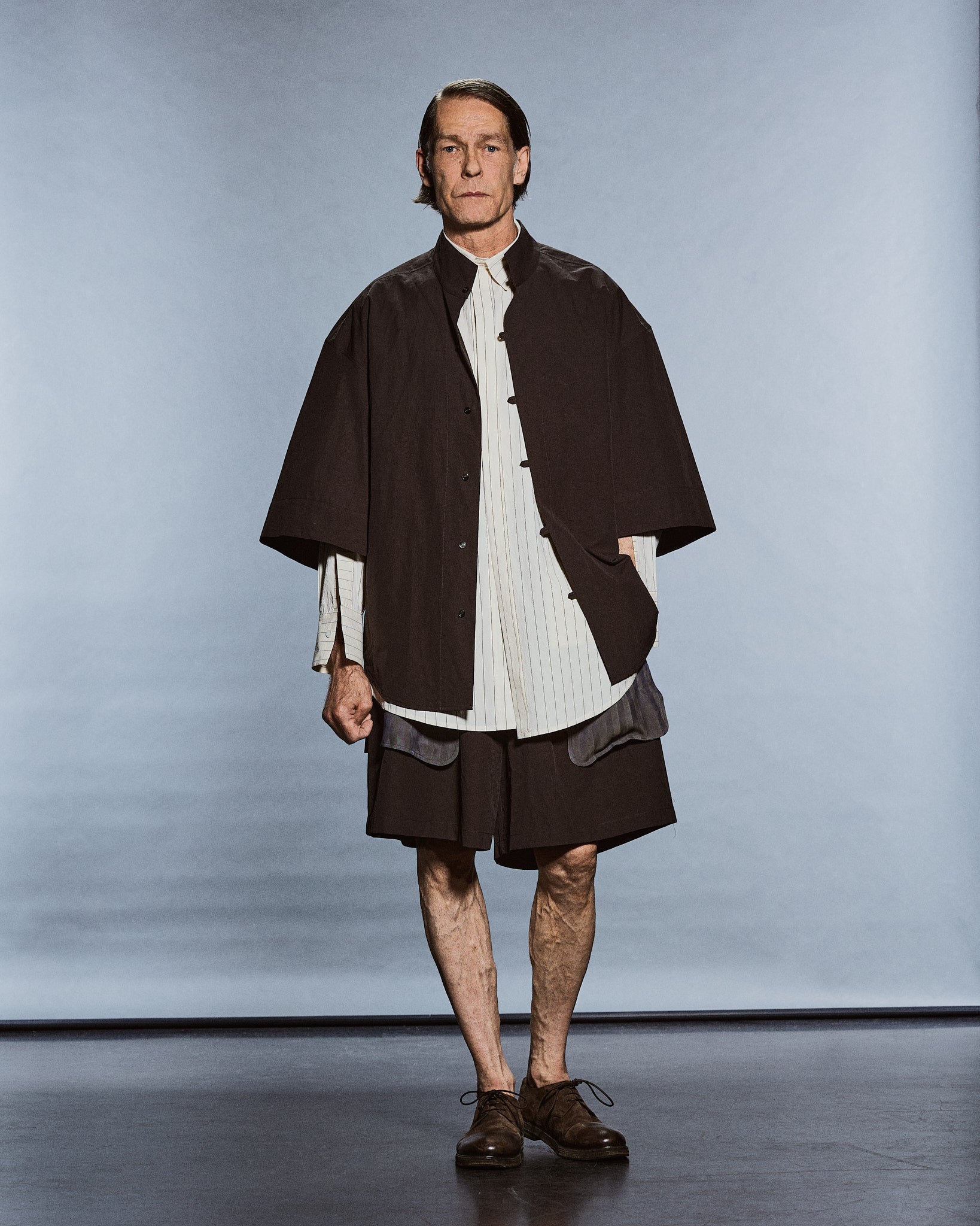 Model in a brown short-sleeve overshirt over a pinstripe shirt and dark shorts — GABRIELSTUNZ APLOMB SS27.