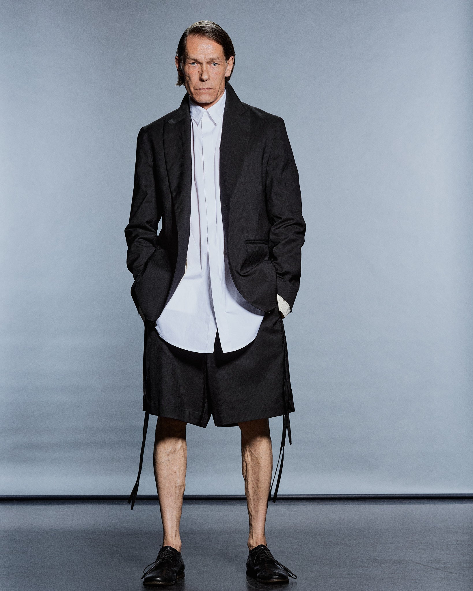 Full-length black tailored blazer over a long white shirt and black shorts with trailing ties — GABRIELSTUNZ APLOMB SS27.